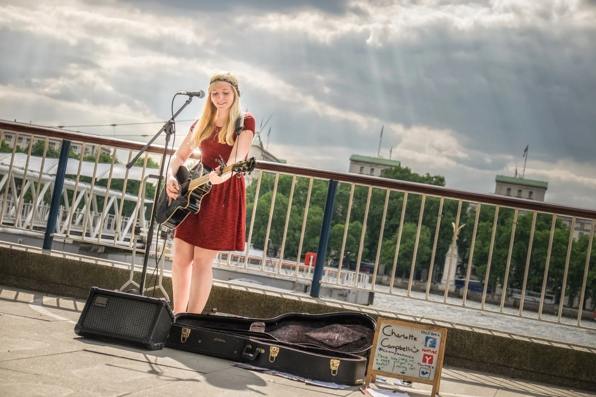 Charlotte Campbell playing guitar in the street before a bridge