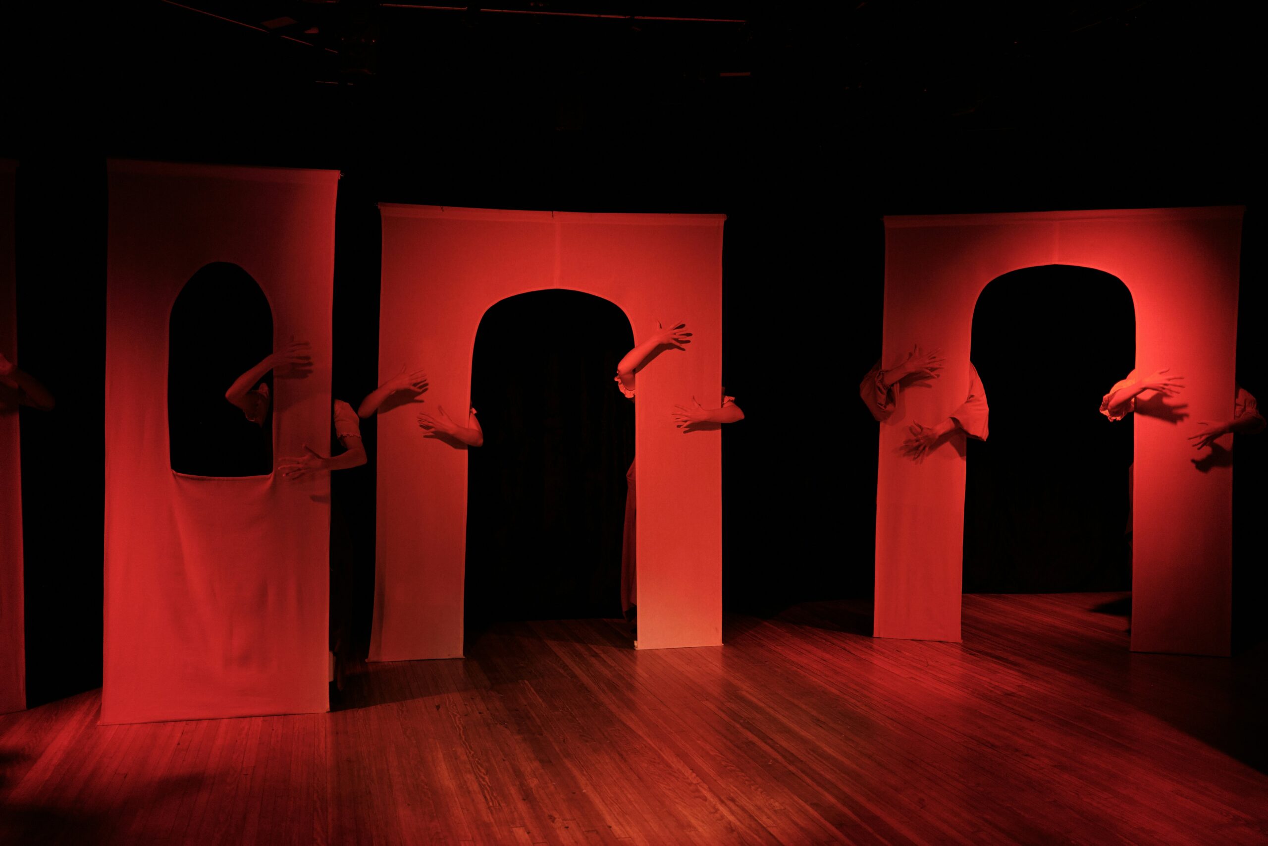 on a stage, three portals, each with hands visible from people carrying them from behind