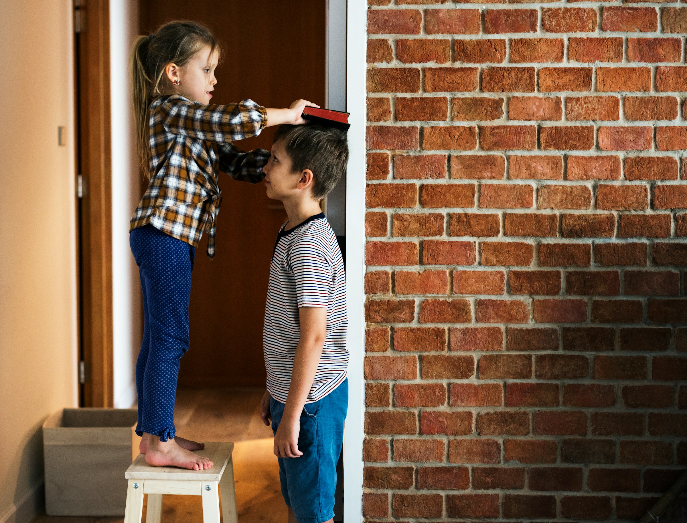 little girl standing on a ladder to check the height of her big brother