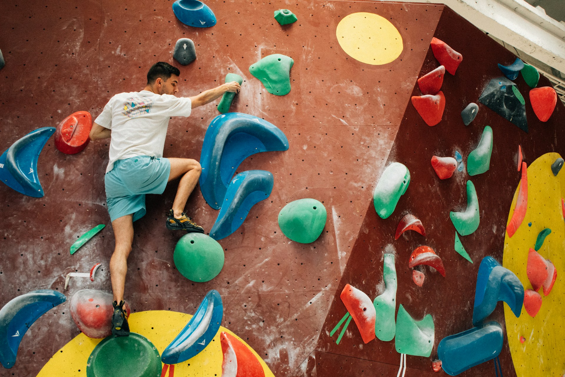 man climbing up an indoor wall with colorful plastic handholds